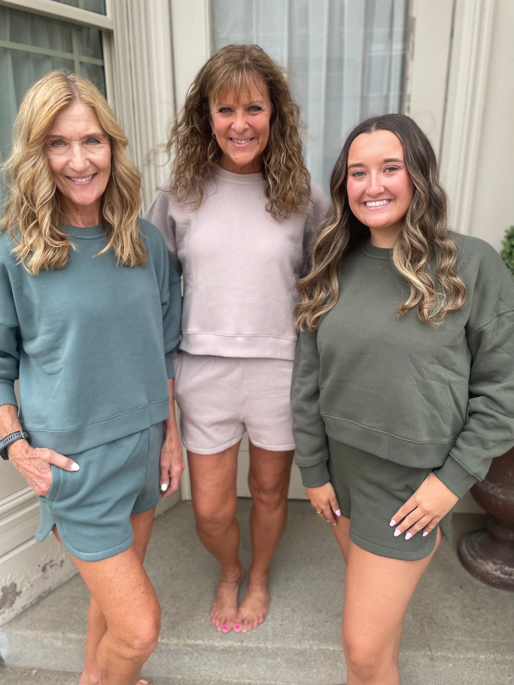 Three women standing together wearing matching outfits in front of a house.