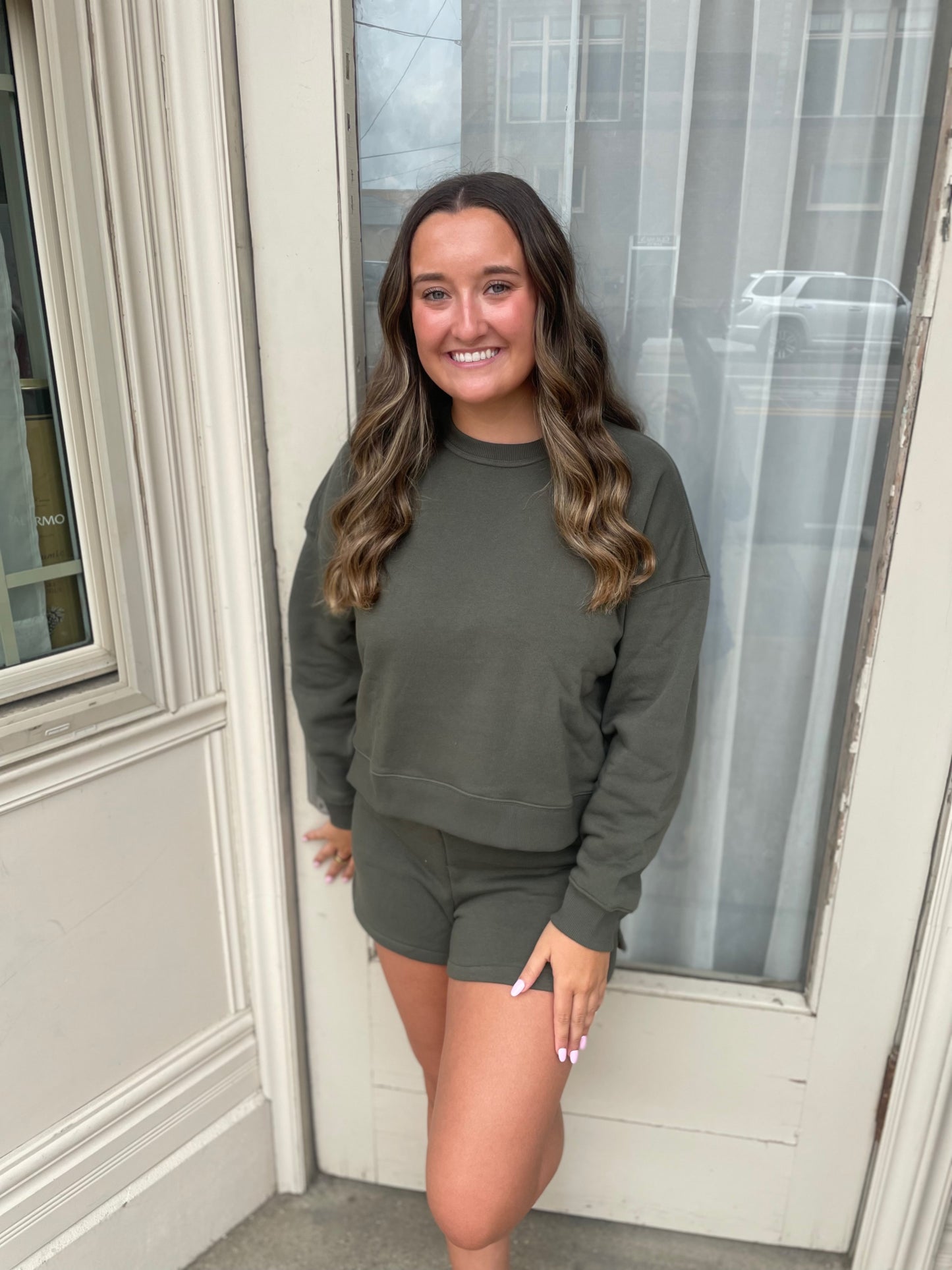 Woman wearing a green sweatshirt and shorts standing in front of a door.