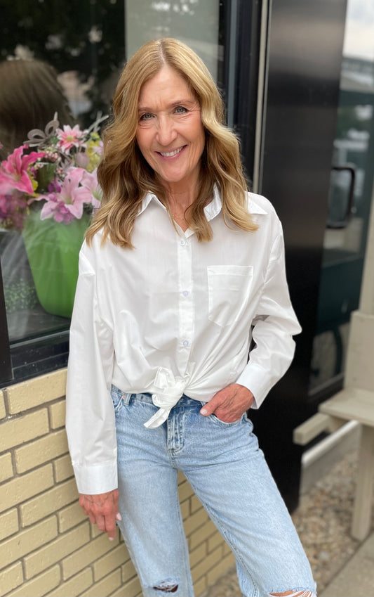 Woman wearing a white shirt and light blue jeans standing outdoors.