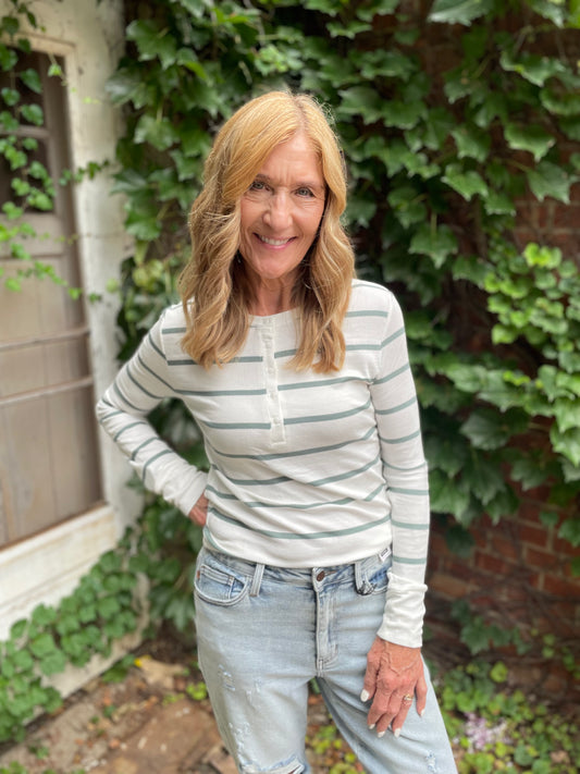 Woman wearing a striped shirt and jeans standing in front of a green ivy-covered wall.