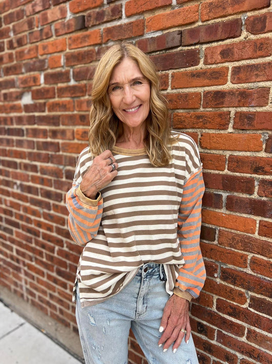 Woman wearing a striped sweater and jeans standing against a brick wall